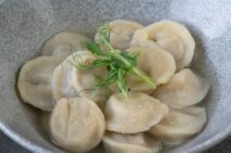 Ljusfärgade kokta dumplings i skål, garnerade med gröna ärtskott